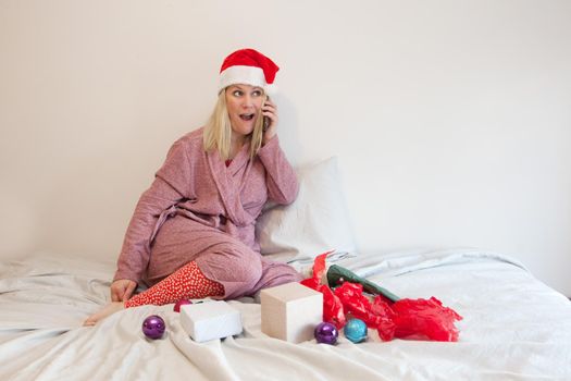 woman on the phone chatting about christmas morning wearing a santa hat and bathrobe