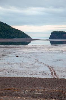 tire tracks lead through mud in low tide near an island on the atlantic ocean 