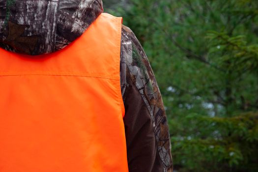 person wearing protective blaze orange vest while in the forest 