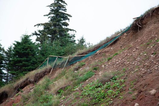  wooden fence with mesh netting has started to fall down the side of a cliff as the rockface erodes 