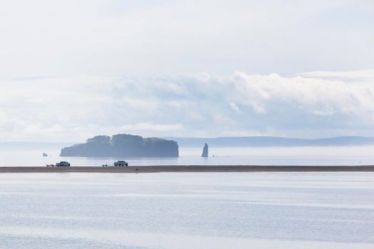 the fog rolls in over a beautiful ocean beach scene with two trucks in the distance 