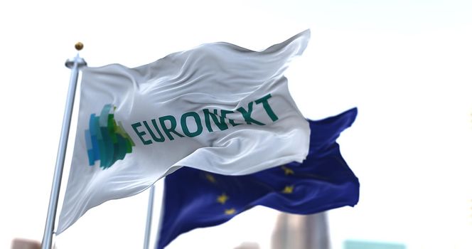 Amsterdam, HOL, April 2021: The Euronext flag flapping in the wind along with the European Union flag blurred in the background. Euronext is a stock exchange in Europe