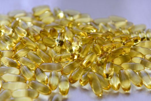 Bunch of omega 3 fish liver oil capsules in pile. Close up of big golden translucent pills texture. Healthy every day nutritional supplement. Top view.