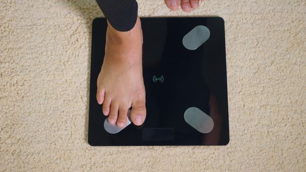 Asian young woman leg stepping standing on floor electric scales, female working out at home in living room, female stand on digital weighing machine. Healthy weight loss control concept, slow motion