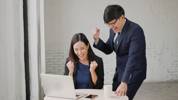 Yes! Happy excited successful, Asian businessman and woman smile workstation triumphing with raised hands together with laptop computer, woman success project online winner