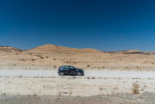 A car in the middle of the desert. A view from the crater in the Ramon Crater. Arid desert view. White sands and a horizon of blue skies. Negev, Israel. High quality photo