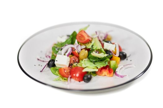 Close up of salad with tomatoes,olives, feta cheese, onion and fresh greens in white background. Concept of delicious vegetables with healthy ingredients for weight loss.