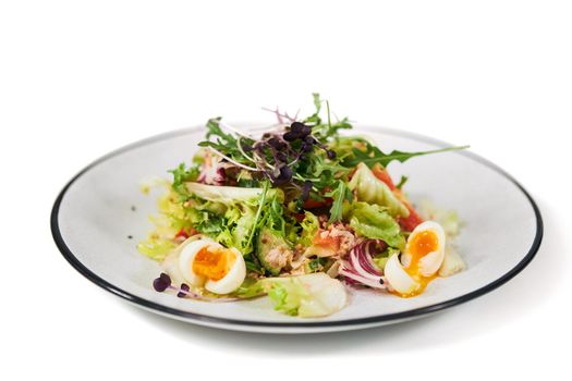 Close up of appetizing salad with eggs and fresh vegetables in modern plate on white background. Concept of dieting salad with vitamins for body weight maintenance.