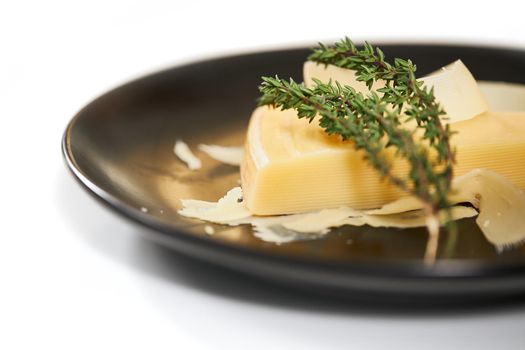 Close up of delicious parmesan with sprig of rosemary in modern black plate on white background. Concept of appetizing cheese with healthy ingredients for lunch or dinner. 