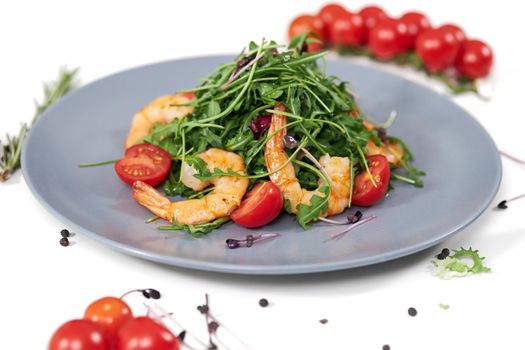 Close up of large modern blue plate with juicy shrimps,tomatoes and fresh arugula on white background. Concept of proper nutrition to maintain body weight. 