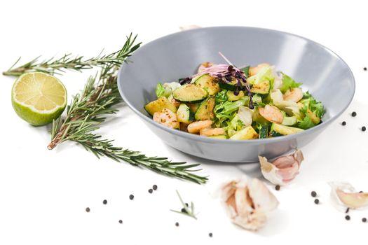 Close up of modern elegant blue plate with juicy vegetables salad with shrimps and zucchini,garlic on white background. Concept of proper nutrition to maintain body weight. 