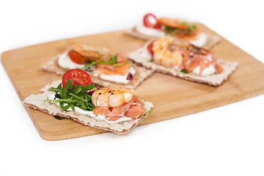 Close up of appetizing diet breads with shrimp, salmon and tomatoes,arugula on wooden board. Concept of tasty and healthy food for weight maintenance and weight loss.