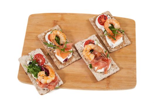 Top view close up of delicious sandwiches with shrimp, salmon and tomatoes on wooden board. Concept of appetizing toasts with healthy ingredients to support the figure. 