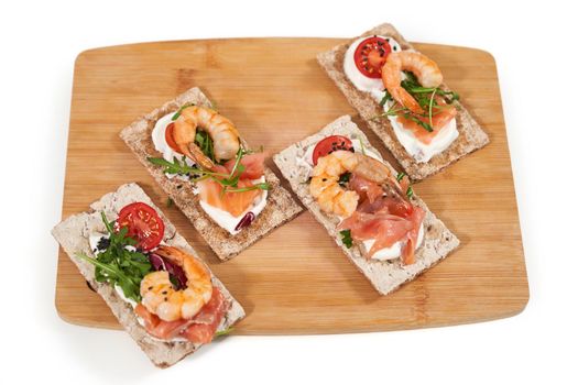 Top view close up of four appetizing sandwich of diet breads with shrimp, salmon and tomatoes,arugula on wooden board. Concept of delicious healthy toasts with fresh seafood. 