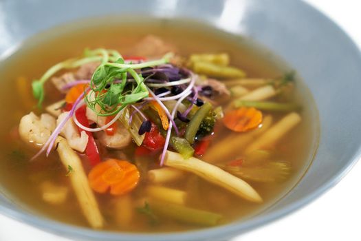 Close up of hot delicious healthy vegetables soup with different fresh greens. Concept of eating appetizing soup with carrots, potatoes, beans,cauliflower and natural seasoning. 