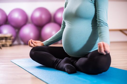 Close up stomach of a pregnant woman meditating in gym,Padmasana-Lotus position