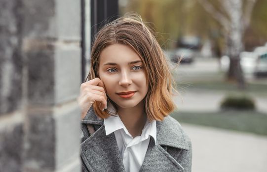 Face portrait of an attractive young woman in a gray coat against the background of a blurred cityscape