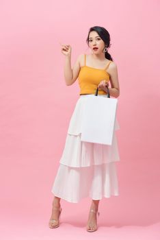 Full length portrait of smiling young woman with shopping bags over pink background.