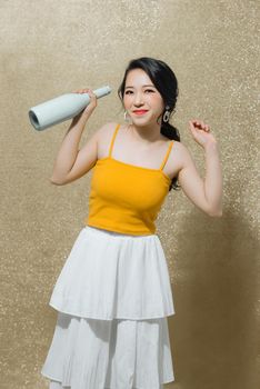 Portrait of sweet, gorgeous young Asian woman with bottle of beverage in hands isolated on bright gold background