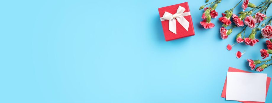 Mother's Day gift. Top view design concept of holiday greeting card with red carnation bouquet on bright blue table background