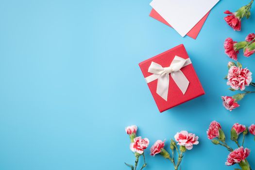 Mother's Day gift. Top view design concept of holiday greeting card with red carnation bouquet on bright blue table background