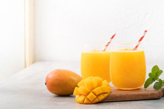 Fresh mango juice. Close up design concept of smoothie cold drink in a glass cup with paper straw on gray table background.