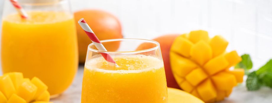 Fresh mango juice. Close up design concept of smoothie cold drink in a glass cup with paper straw on gray table background.