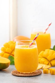 Fresh mango juice. Close up design concept of smoothie cold drink in a glass cup with paper straw on gray table background.