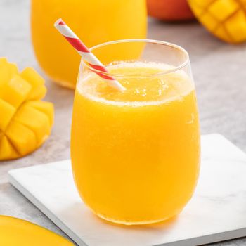 Fresh mango juice. Close up design concept of smoothie cold drink in a glass cup with paper straw on gray table background.