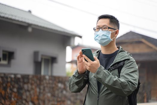 Young backpacker man is traveling alone and using smart phone to find a way with wearing mask, glasses.