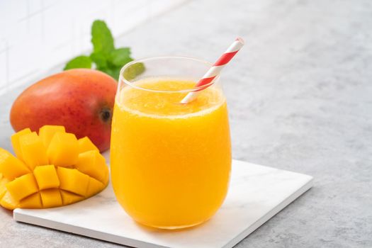 Fresh mango juice. Close up design concept of smoothie cold drink in a glass cup with paper straw on gray table background.