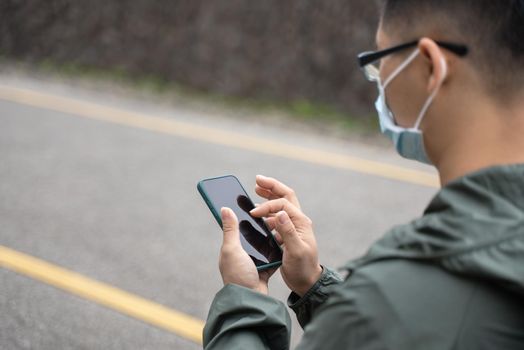 Young backpacker man is traveling alone and using smart phone to find a way with wearing mask, glasses.