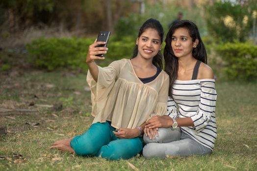 Two beautiful female friends taking selfie with smartphone in outdoors.