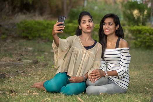 Two beautiful female friends taking selfie with smartphone in outdoors.