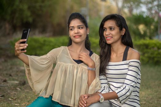 Two beautiful female friends taking selfie with smartphone in outdoors.