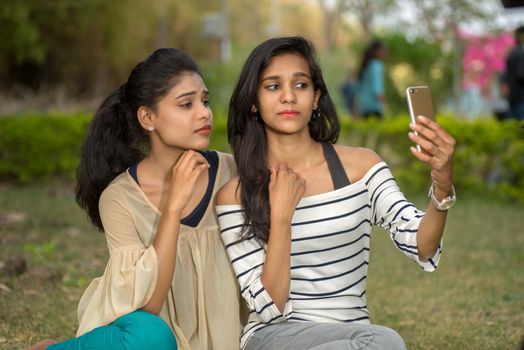 Two beautiful female friends taking selfie with smartphone in outdoors.