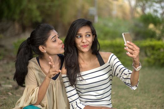 Two beautiful female friends taking selfie with smartphone in outdoors.