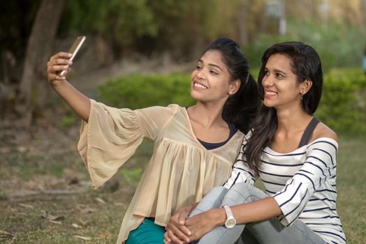 Two beautiful female friends taking selfie with smartphone in outdoors.