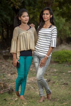 Two young girl friends standing together and having fun in outdoors. Looking at camera.