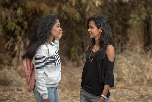 Two young girl friends standing together and having fun in outdoors. Looking at camera.