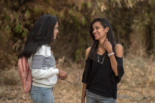 Two young girl friends standing together and having fun in outdoors. Looking at camera.