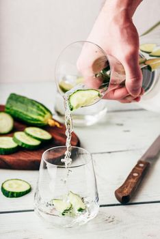 Hand with jug pours infused water with sliced cucumber