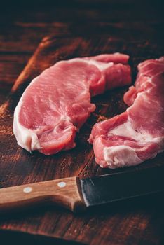 Two pork loin steaks with knife on rustic cutting board