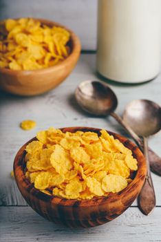 Rustic bowl of corn flakes with spoons and bottle of milk