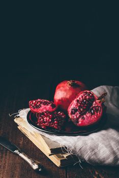 Open pomegranate fruit on metal plate over old books