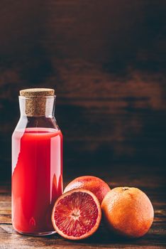 Bottle of blood orange juice with halved fruit on wooden table