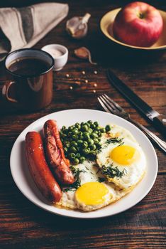 Breakfast with fried eggs, sausages and green peas on white plate