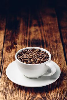 Roasted coffee beans in white cup over rustic wooden surface