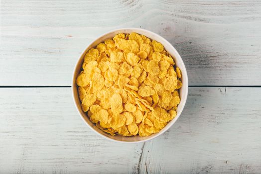 White bowl of corn flakes on a wooden surface