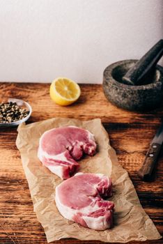 Two pork loin steaks on baking paper with lemon and peppercorn